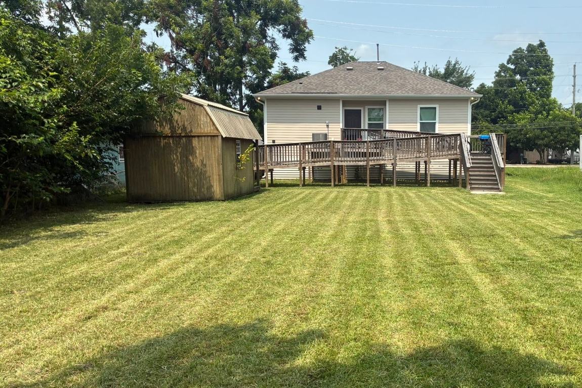 Wide backyard lawn with fresh mowing stripes running toward a raised deck