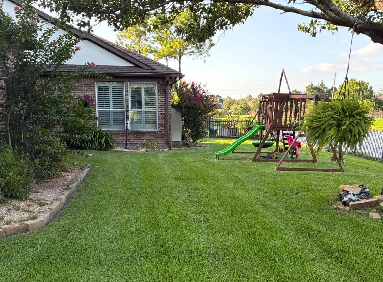 Deep green striped lawn and stone-edged planting beds beside a brick home at golden hour